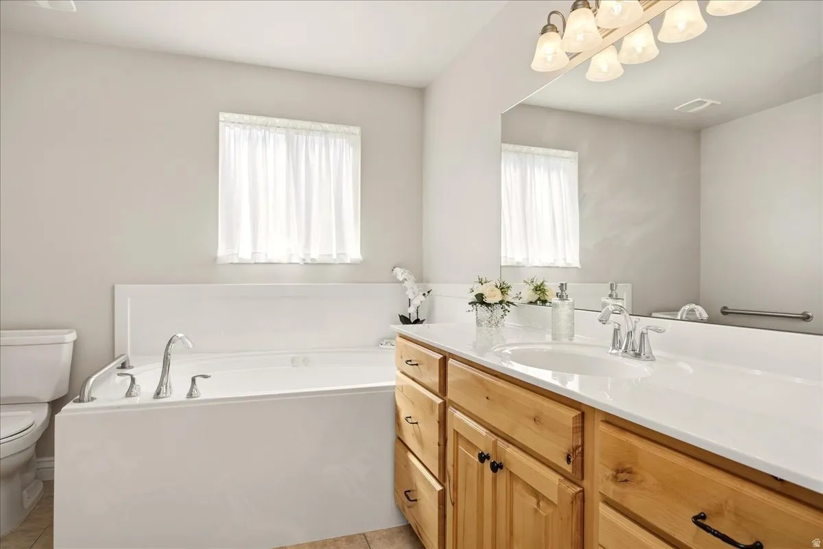 Soaking tub with chrome fixtures, vanity with wood cabinetry, integrated sink with chrome faucet, large vanity mirror, and overhead vanity lighting