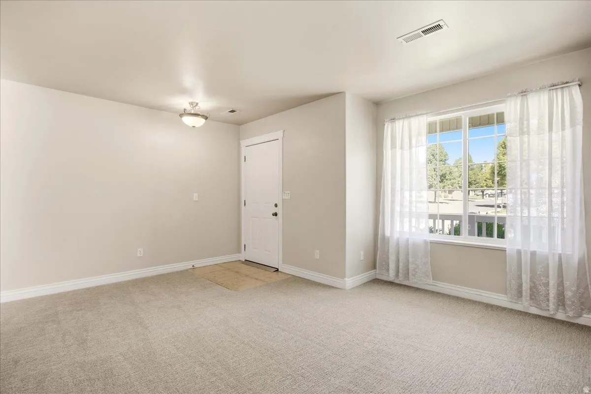 Neutral tone wall paint, light-colored carpet flooring, recessed window with white trim, white paneled door with dark hardware, and a ceiling-mounted light fixture