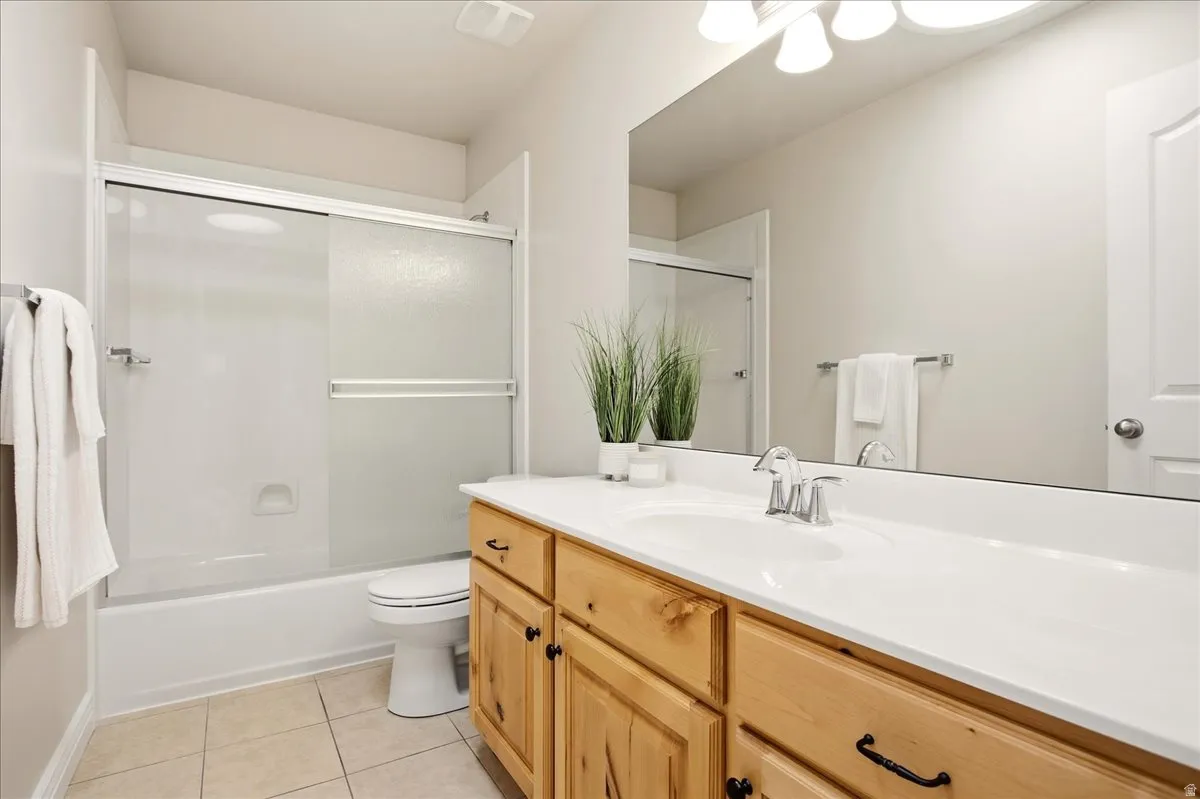 Bathroom featuring a tub-shower combination with sliding glass doors, a single vanity with wood cabinetry, an integrated sink, and a wall-mounted mirror