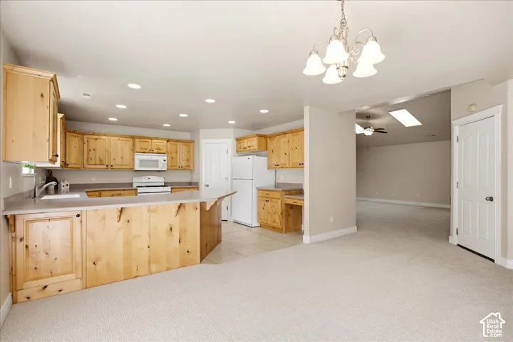 Kitchen featuring light wood cabinetry, white appliances, and a peninsula with countertop seating