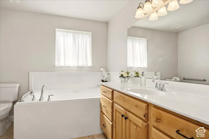 Soaking tub with chrome fixtures, vanity with wood cabinetry, integrated sink with chrome faucet, large vanity mirror, and overhead vanity lighting