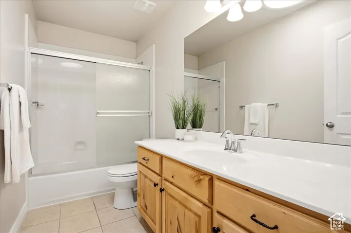 Bathroom featuring a tub-shower combination with sliding glass doors, a single vanity with wood cabinetry, an integrated sink, and a wall-mounted mirror