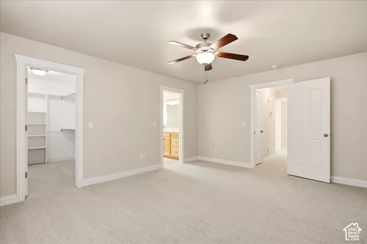 Expansive carpeted room featuring a ceiling fan with light fixture, walk-in closet with built-in shelving