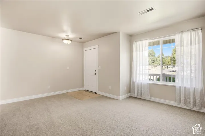 Neutral tone wall paint, light-colored carpet flooring, recessed window with white trim, white paneled door with dark hardware, and a ceiling-mounted light fixture