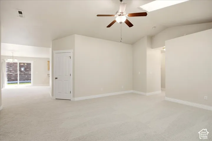 Vaulted ceilings with a skylight, ceiling fan, and light-toned carpeting throughout