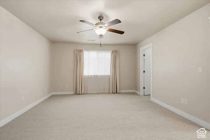 Primary bedroom featuring a ceiling fan with integrated lighting, a window with sheer and solid curtains, and light-toned walls