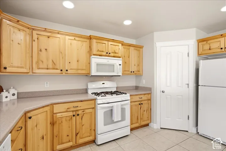 Wood-finish cabinetry with black hardware, white appliances, solid surface countertops, recessed lighting, and tile flooring