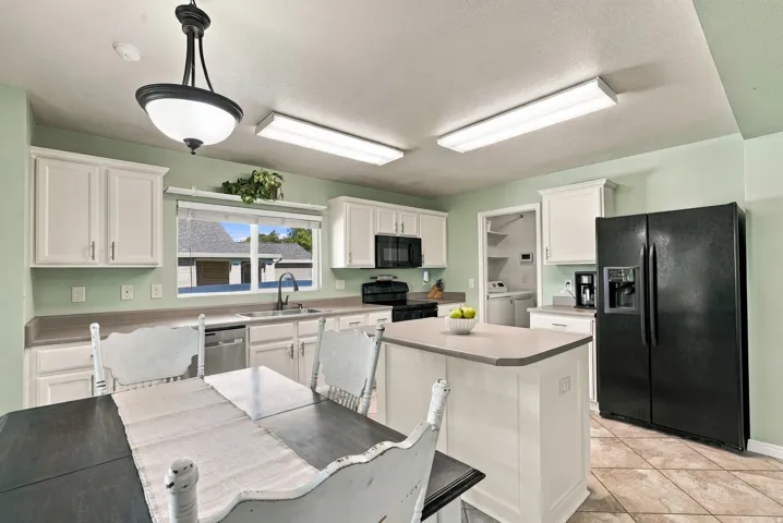 White cabinetry, countertop island, black appliances, tiled flooring, and a window above the sink