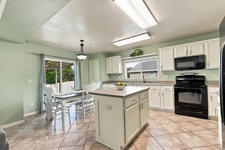 Kitchen features a central island, white cabinetry, dark countertop, tile flooring, and a sliding glass door