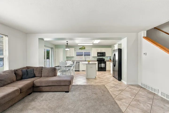 Open concept living area with carpet flooring, recessed lighting, and a wood-finish staircase