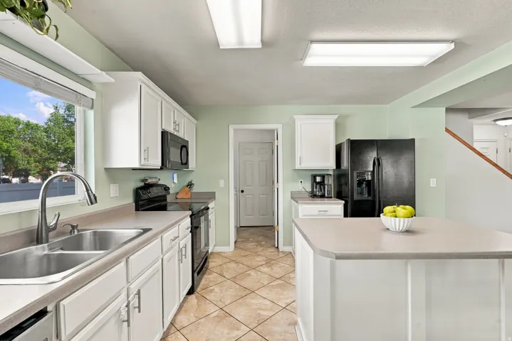 Kitchen featuring white cabinetry, a double basin stainless steel sink, black appliances, a central island, and tiled flooring