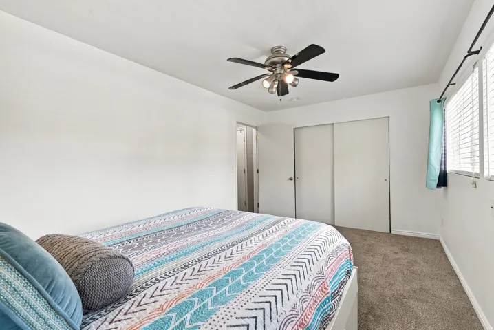 Ceiling fan with integrated lighting, carpeted flooring, window with blinds, and a closet with sliding doors