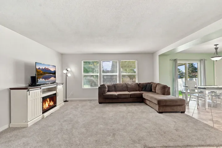 Spacious living area featuring light gray wall paint, light gray carpeting, and multiple windows