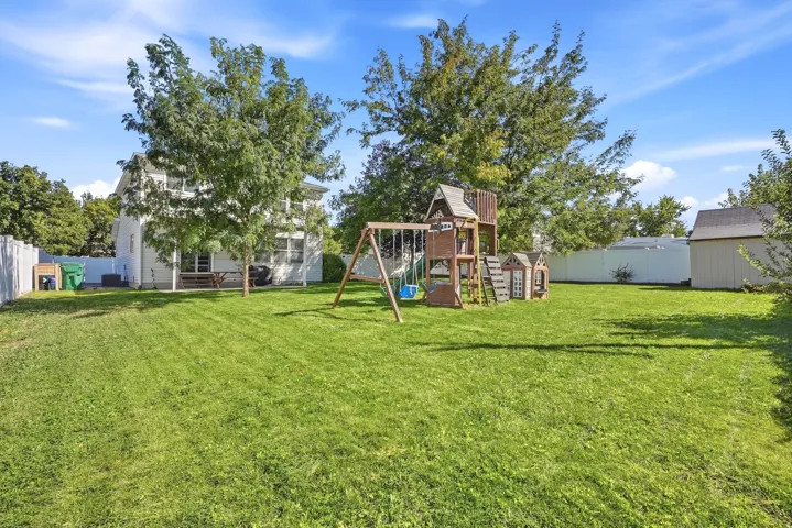 Expansive rear yard featuring a wooden playset, a utility shed, and a privacy fence