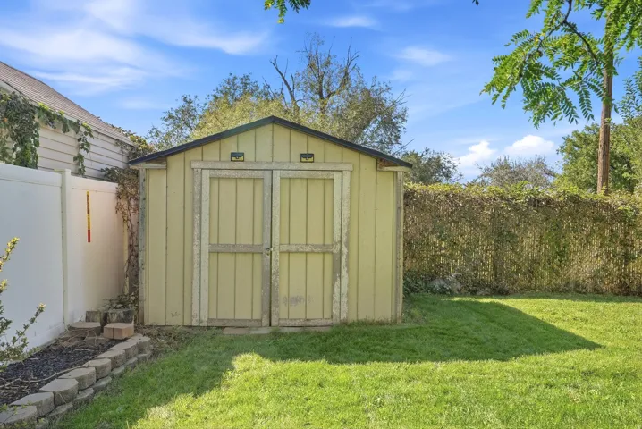 Detached storage shed with double doors, established lawn, privacy fencing, and mature perimeter landscaping