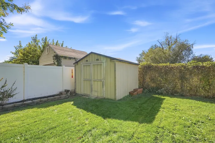 Expansive lawn featuring a storage shed, vinyl privacy fence, and mature perimeter hedging
