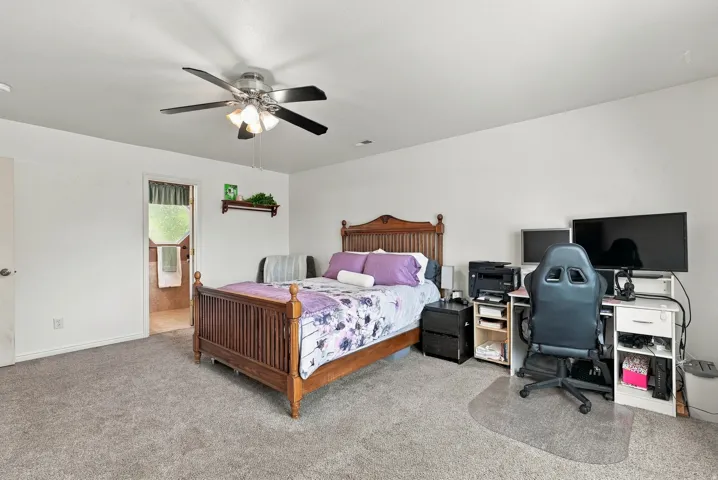 Carpeted room featuring a ceiling fan with light fixture and a doorway to a tiled area