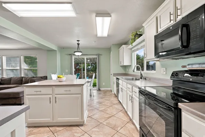 Kitchen featuring white cabinetry, black appliances, a center island with storage, and tiled flooring