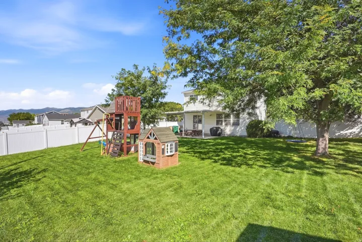 Expansive backyard with a manicured lawn, established shade trees, and a full white privacy fence