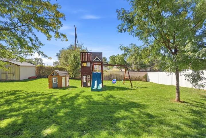 Expansive grassy yard with mature trees and a white privacy fence