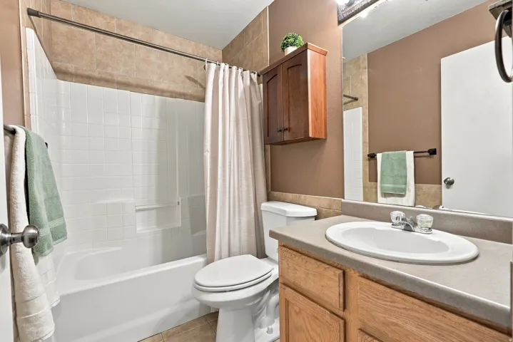 Full bathroom featuring a white tub-shower combination with tiled surround, a vanity with an integrated sink and light wood-finish cabinetry, a wall-mounted wooden cabinet, and tile flooring