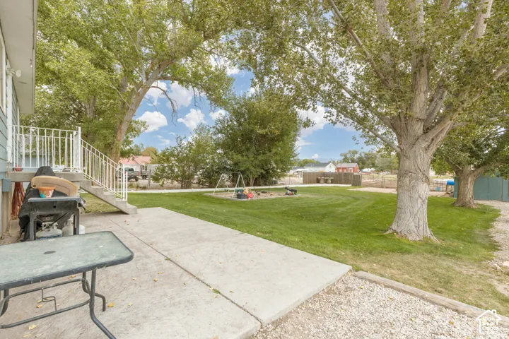 Expansive backyard featuring a manicured lawn, mature shade trees, and a concrete patio