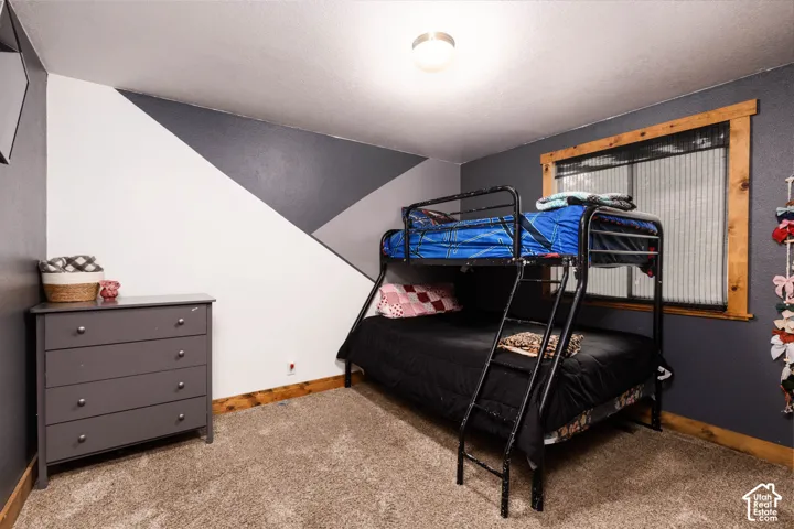 Carpeted room with a ceiling-mounted light fixture, wood-finish window trim, and a patterned accent wall