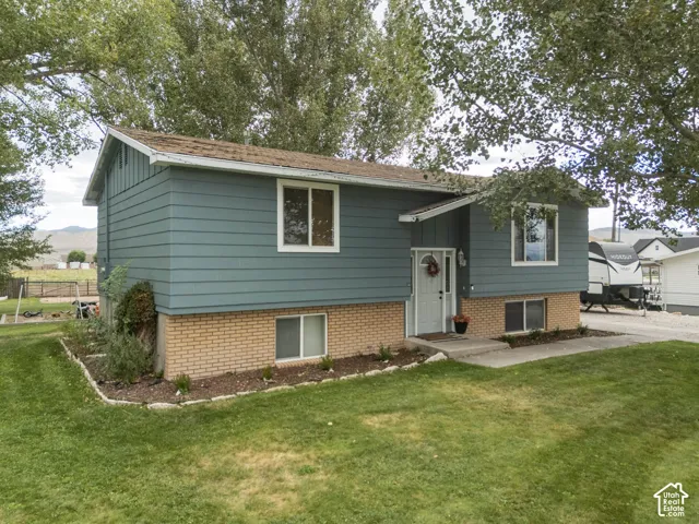 Exterior featuring blue siding, a brick foundation, mature trees, a concrete walkway, and a landscaped front yard