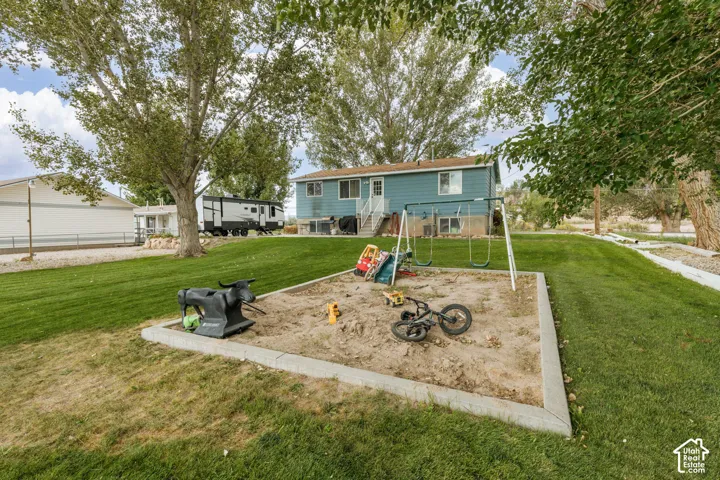Expansive grassy yard featuring a sand play area with concrete edging, mature trees, and a swing set