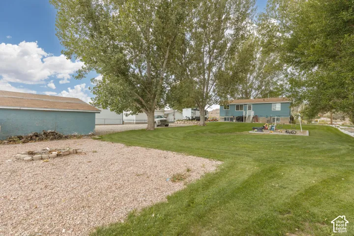Expansive gravel area with a stone fire pit, bordered by a substantial grassy yard
