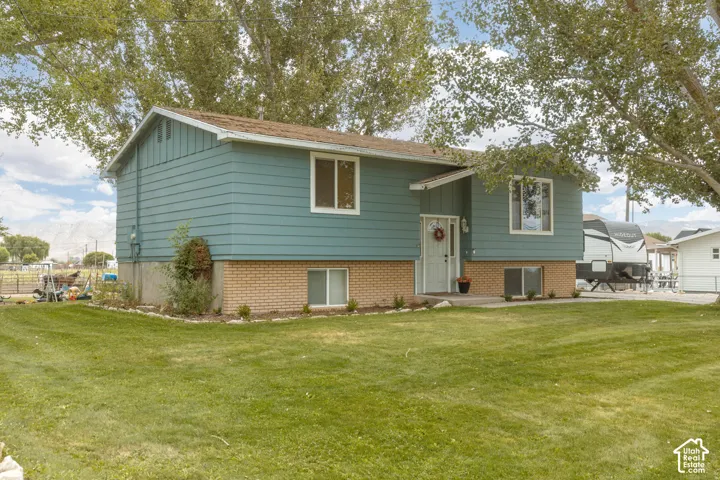 Split-level residence featuring light blue siding, a brick foundation, and a white entry door