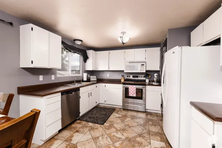 Kitchen featuring white cabinetry, dark countertops, stainless steel appliances, and patterned tile flooring