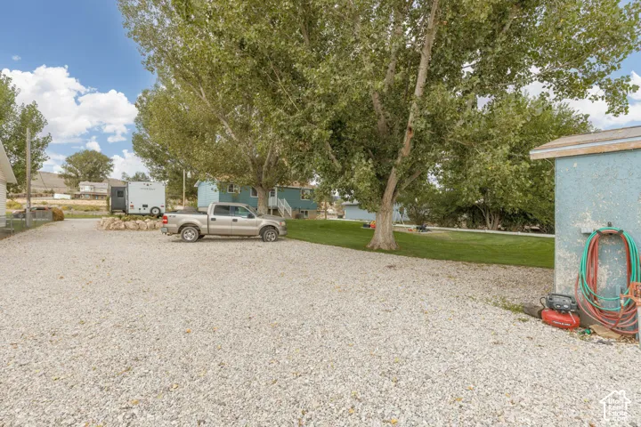 Gravel drive and parking area with a separate storage shed, mature trees, and a grassy yard