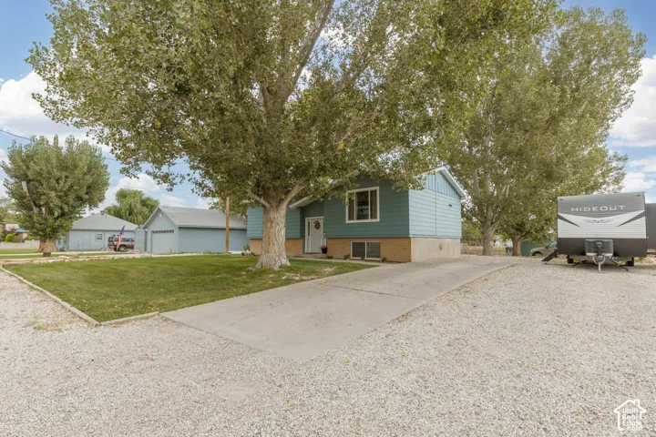 Siding exterior, established trees, concrete driveway, gravel parking area, and green lawn