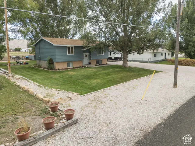 Split-level exterior with blue siding, a gravel driveway, a manicured lawn, and mature trees