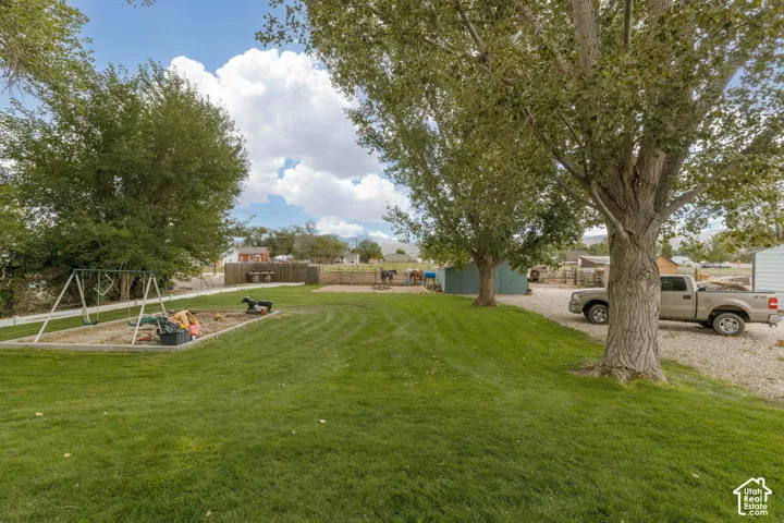 Expansive grassy lawn with established trees, a fenced-in sandbox, and a swing set