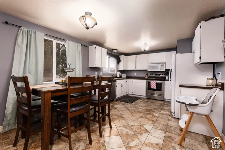 Kitchen featuring white cabinetry, stainless steel appliances, tiled flooring, and a large window