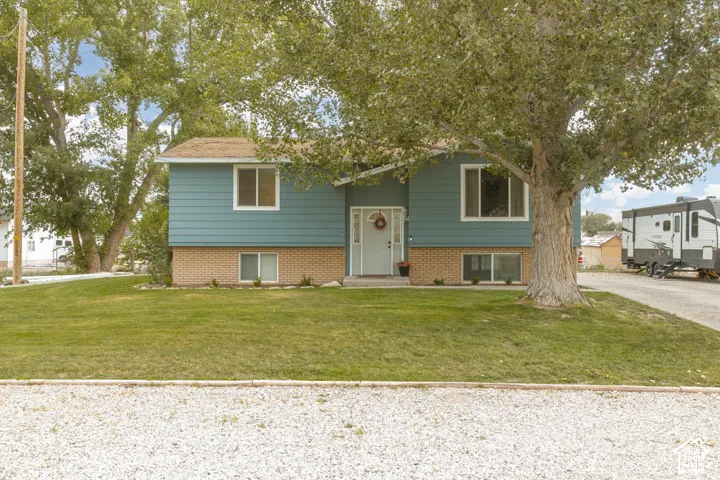 Split-level residence featuring blue siding, brick foundation, and a light-colored front door
