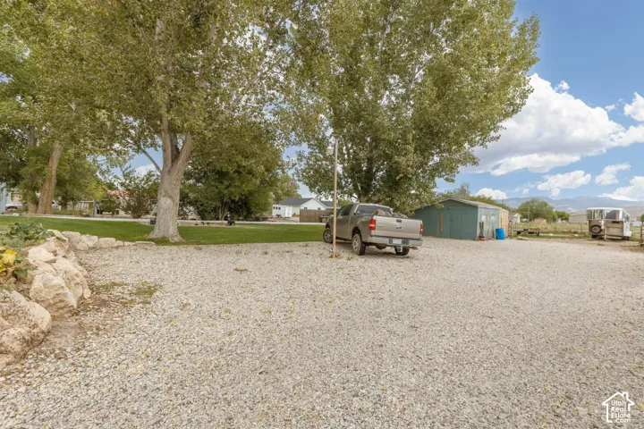 Gravel parking area, mature trees, green outbuilding, and visible mountain range