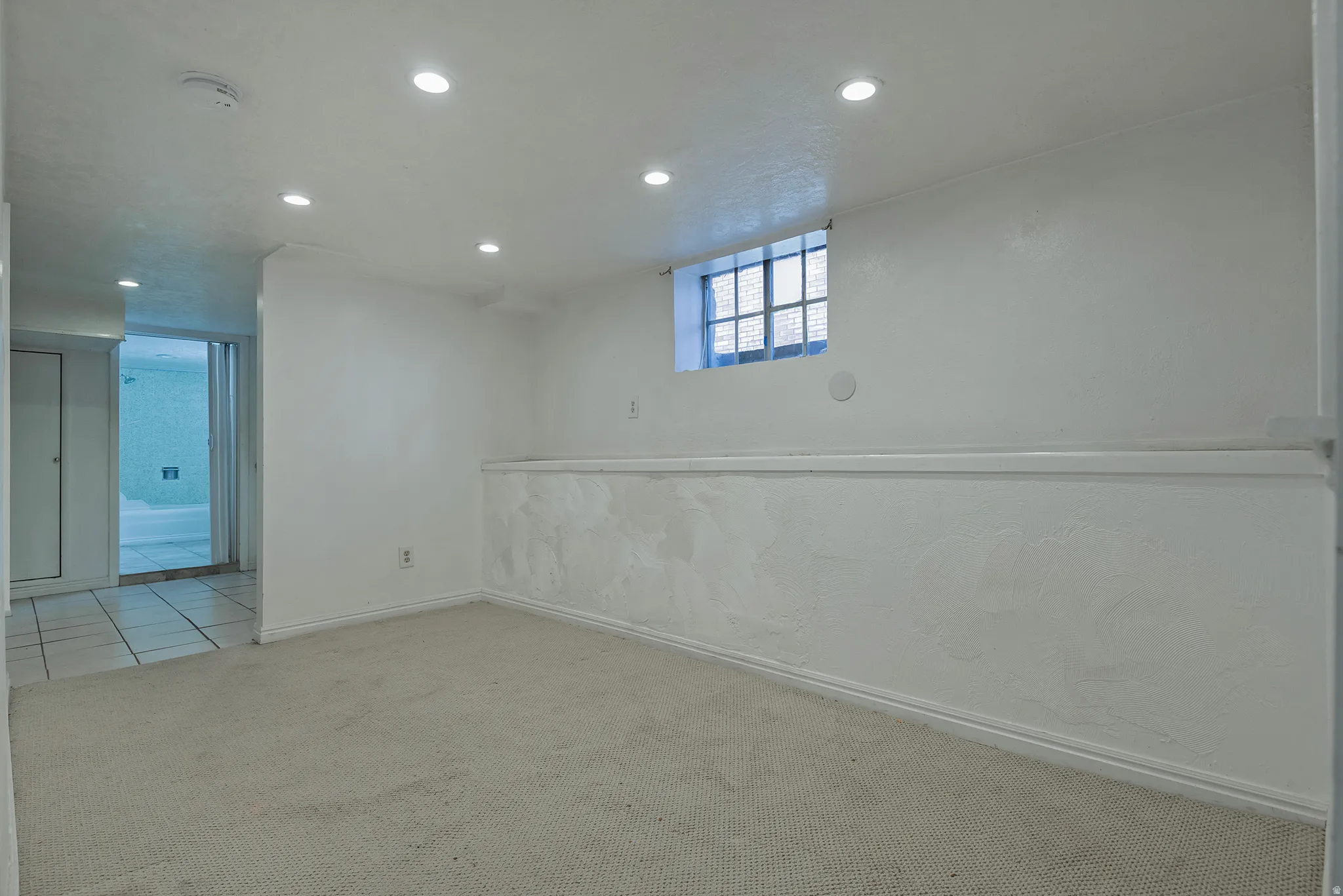 Recessed ceiling lighting, textured wall finish, and a window with security bars