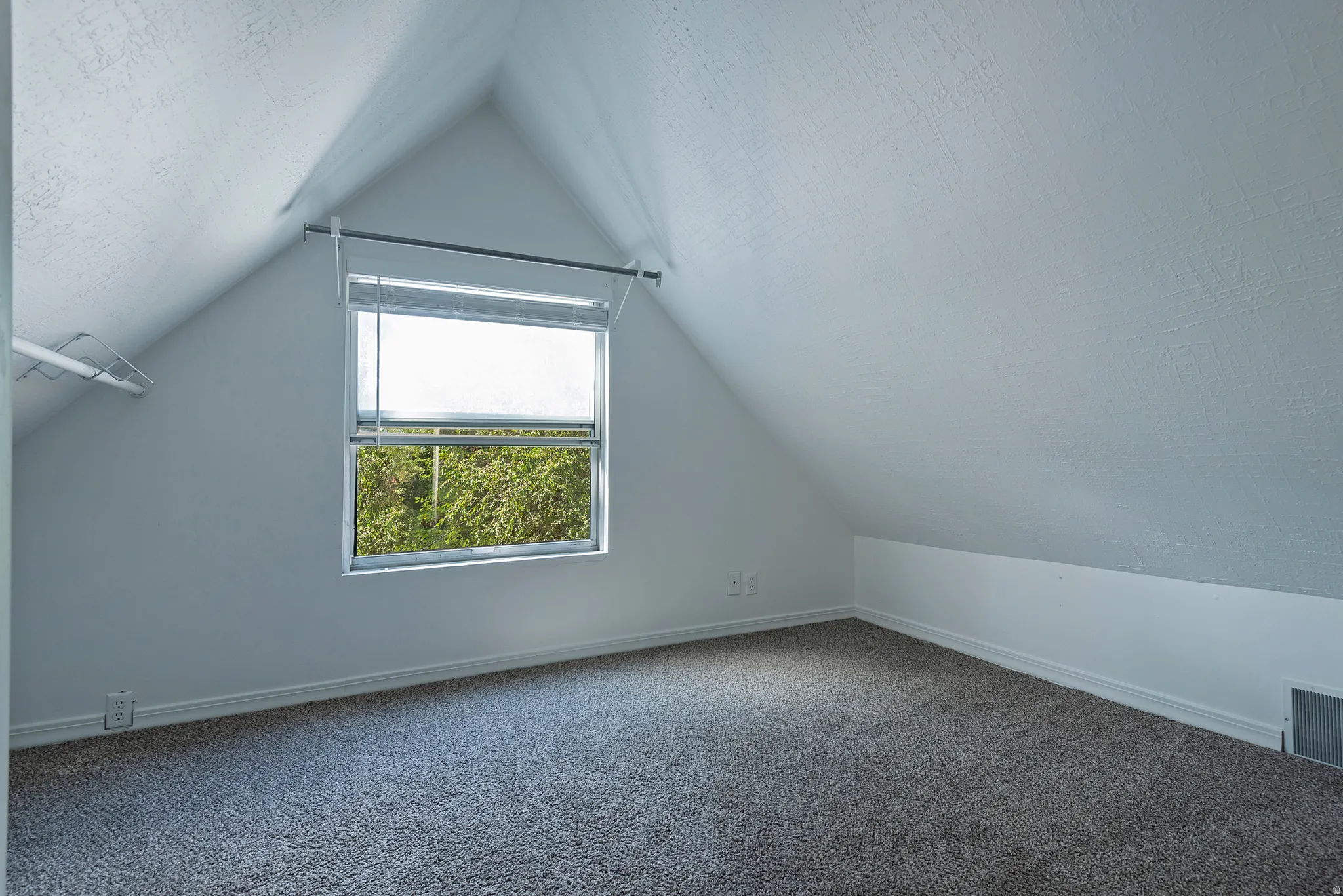 Attic space featuring sloped ceilings, a window with blinds, and gray carpeting