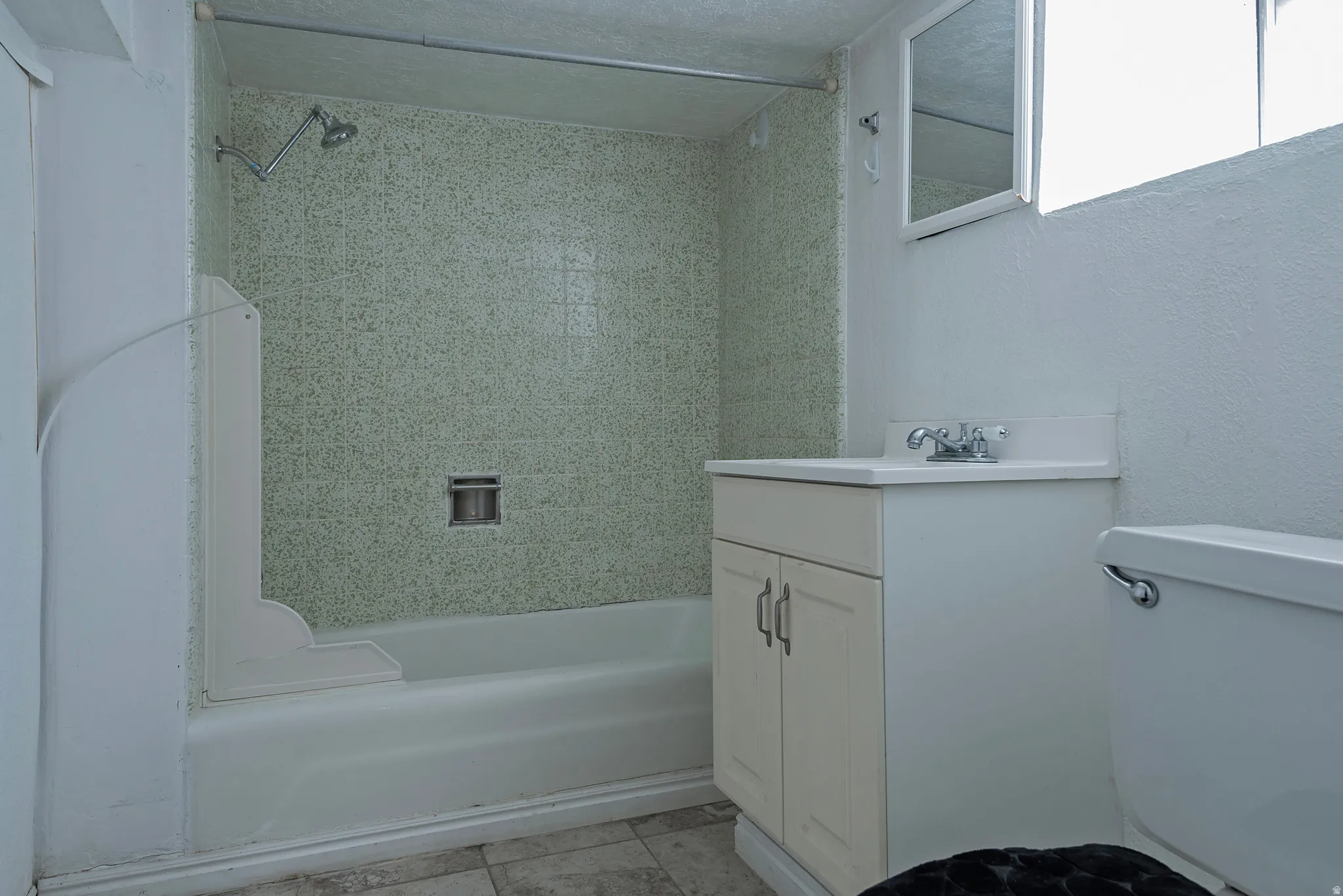 Bathtub with a shower fixture, wall-mounted mirror, white vanity with an integrated sink, and a toilet