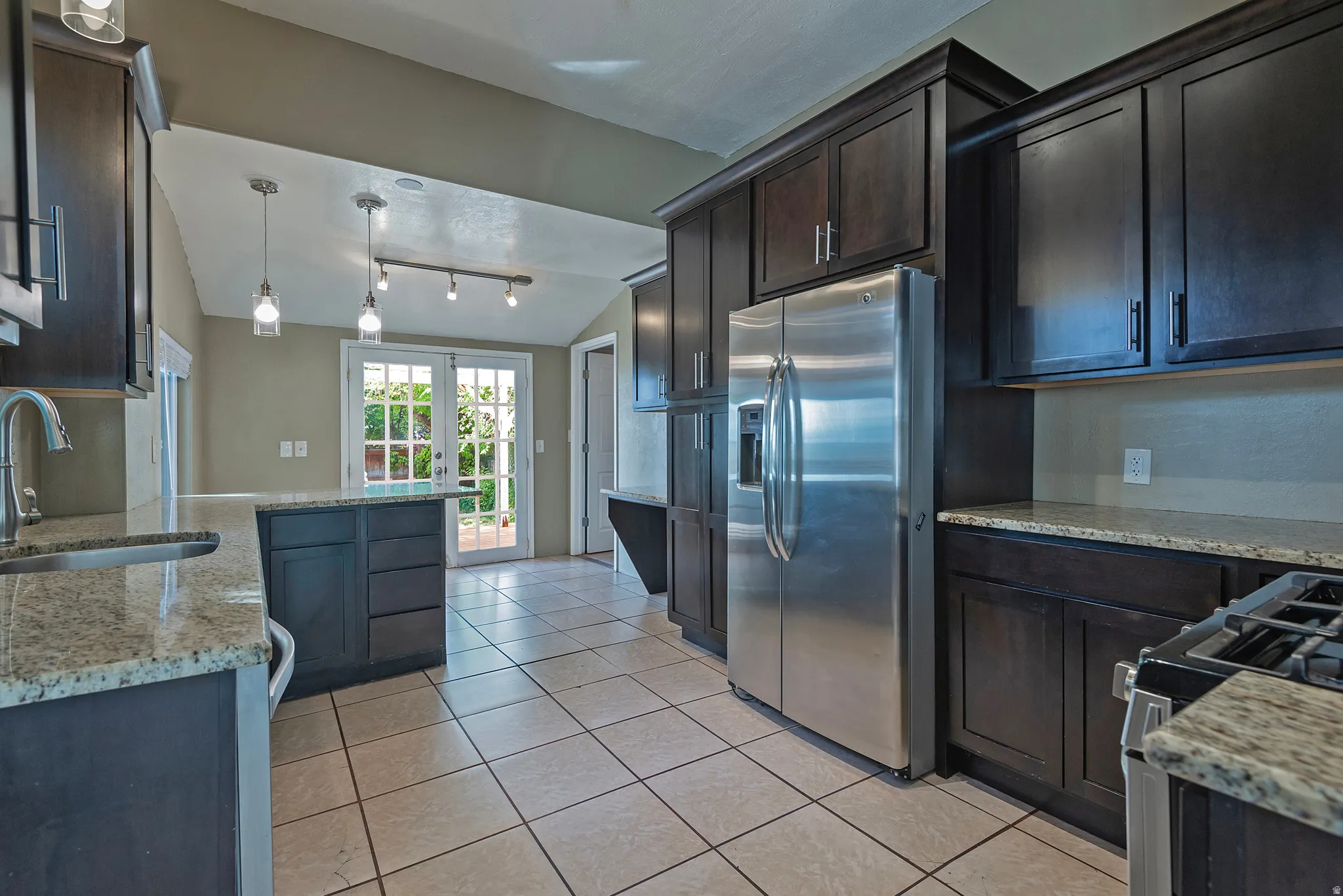 Contemporary kitchen featuring dark wood-finish cabinetry, granite-style countertops, stainless steel appliances, and tile flooring