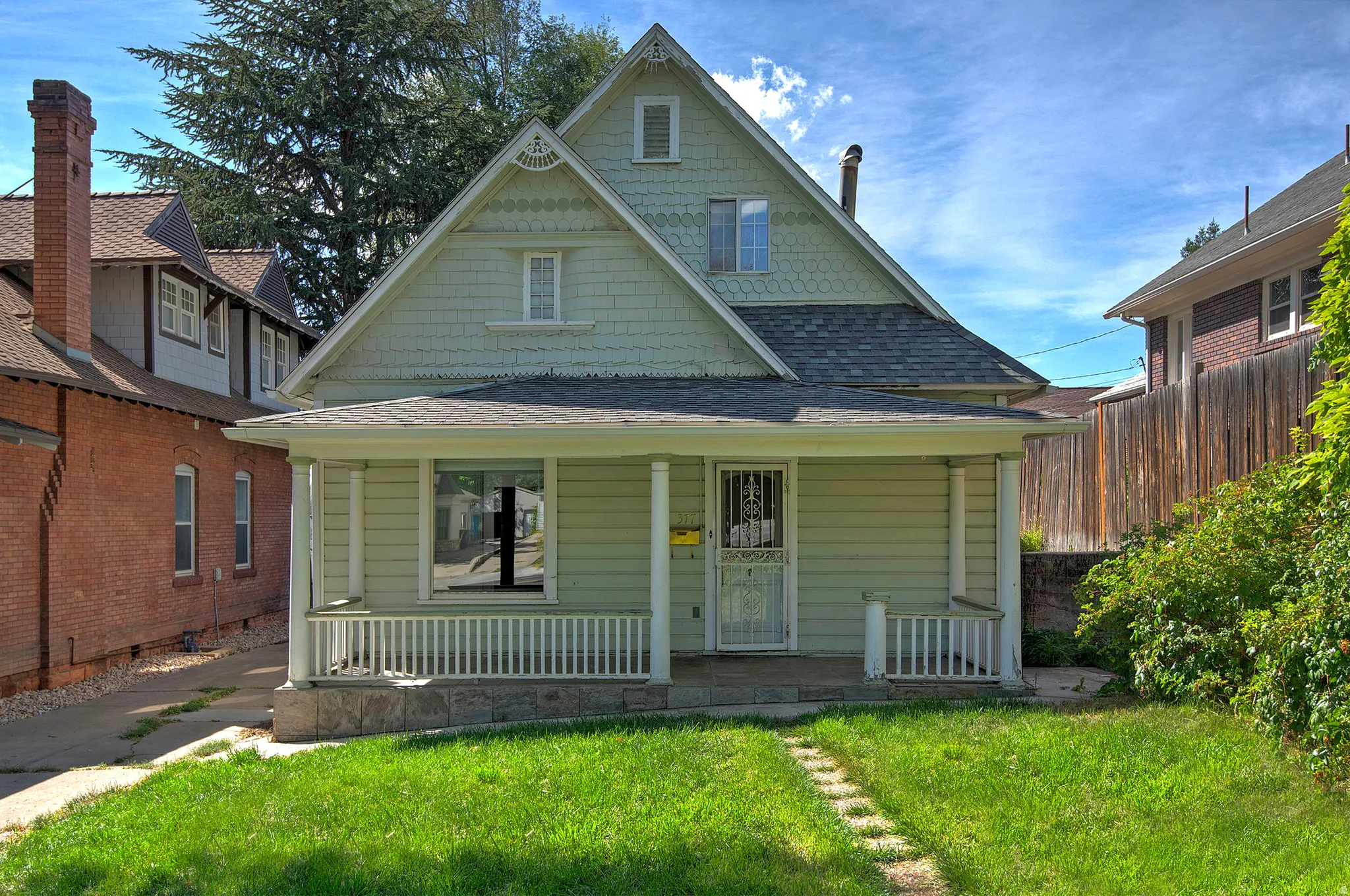 Gabled roofline with decorative shingles, front porch with columns and railing, horizontal siding, and a grass lawn