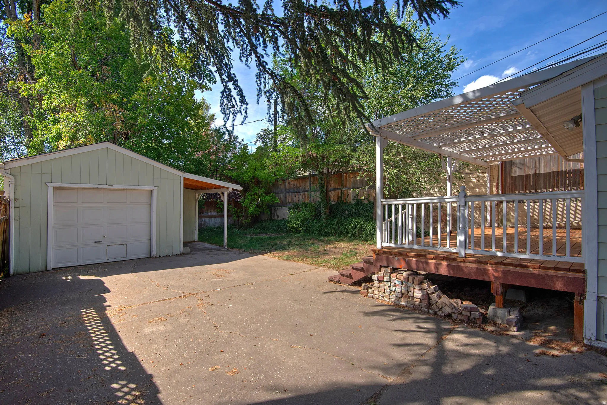 Detached garage with covered entryway, concrete driveway, and elevated wood deck with white lattice pergola and railing