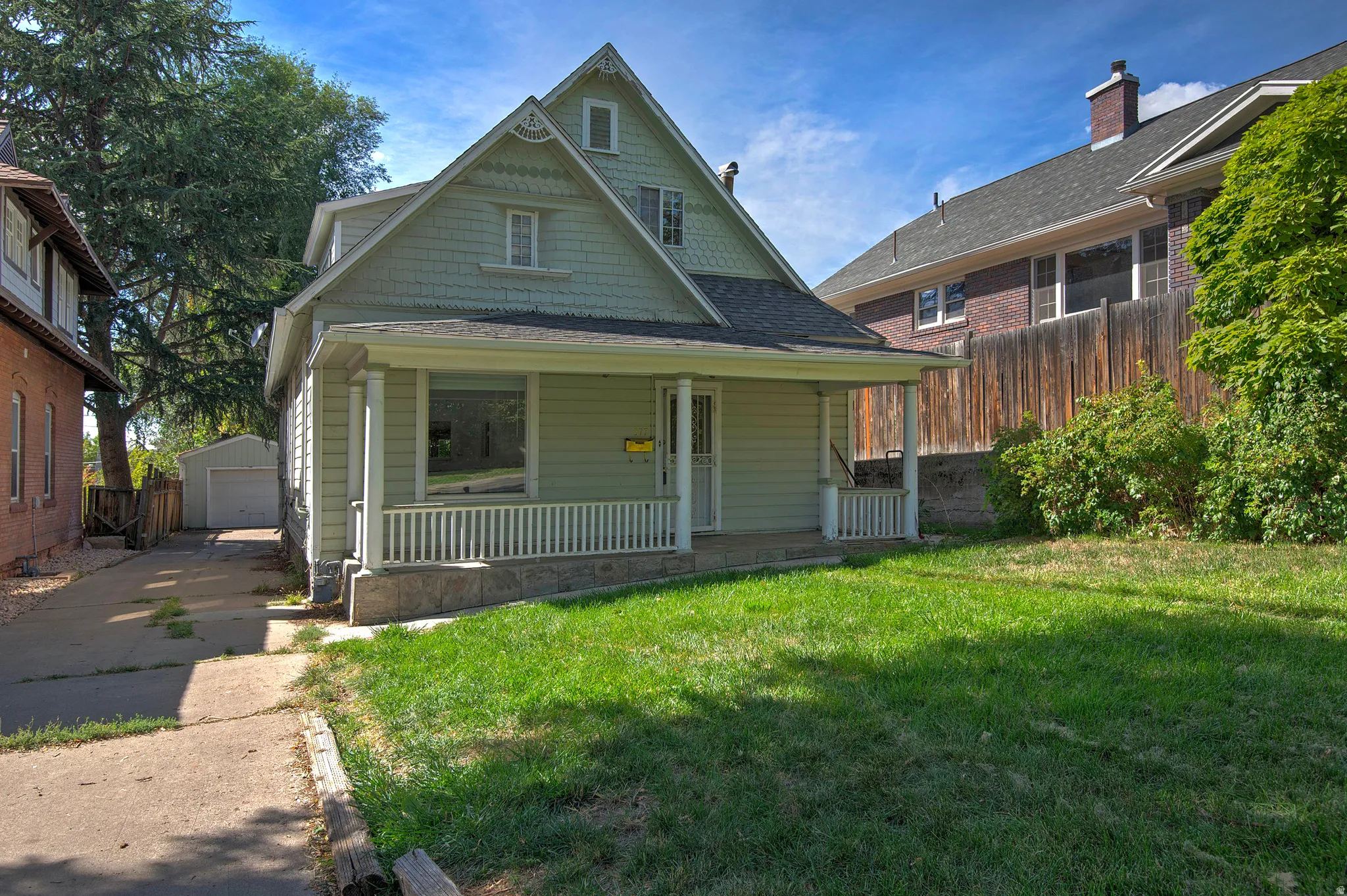Gabled facade featuring shake siding, a covered porch with white railing, and a stone foundation