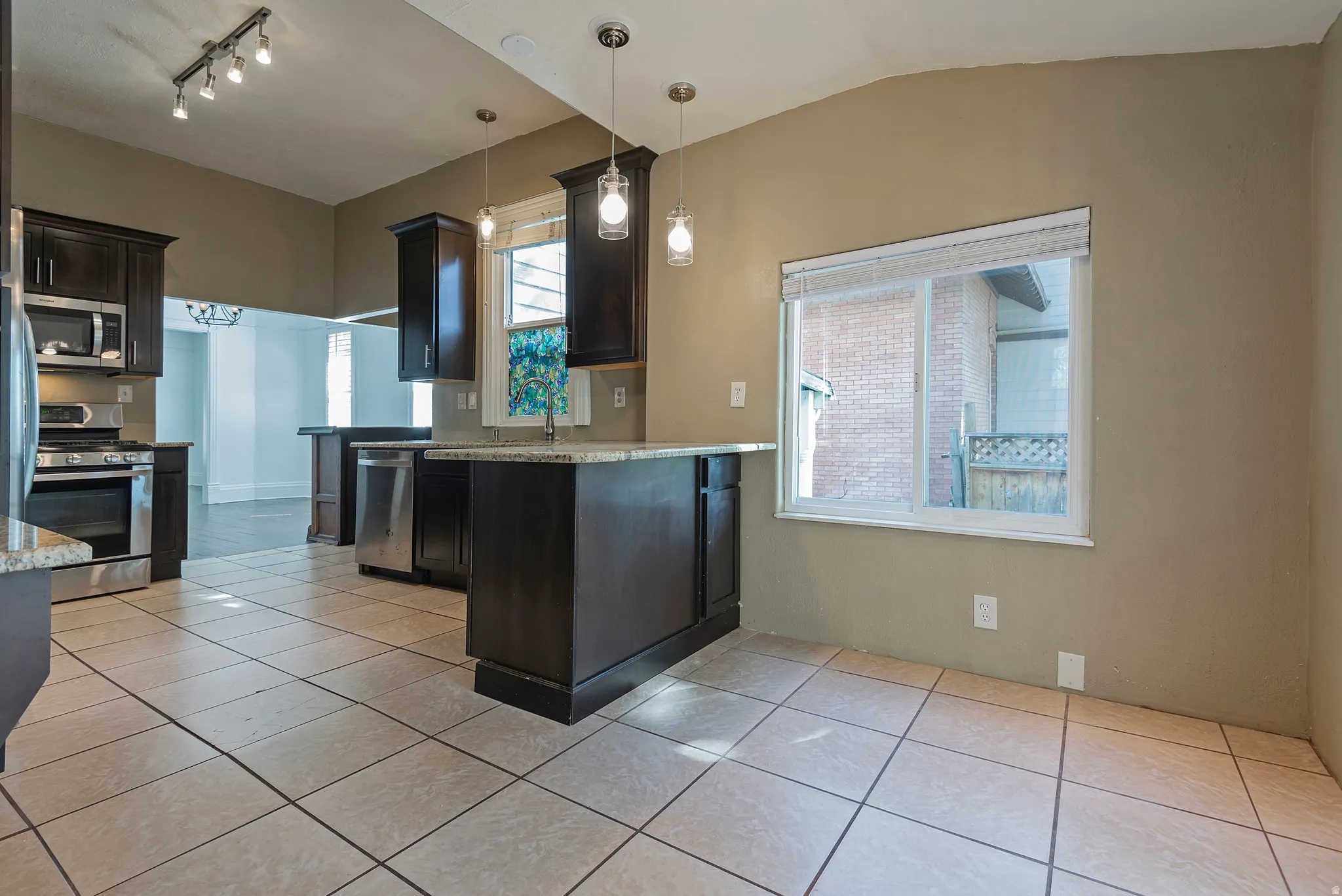 Kitchen with dark wood cabinetry, stainless steel appliances, light-toned tile flooring, and pendant lighting