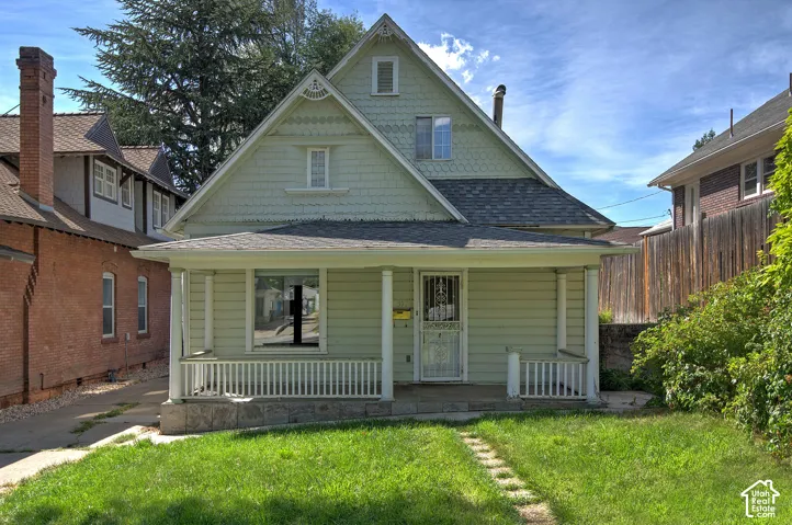 Gabled roofline with decorative shingles, front porch with columns and railing, horizontal siding, and a grass lawn