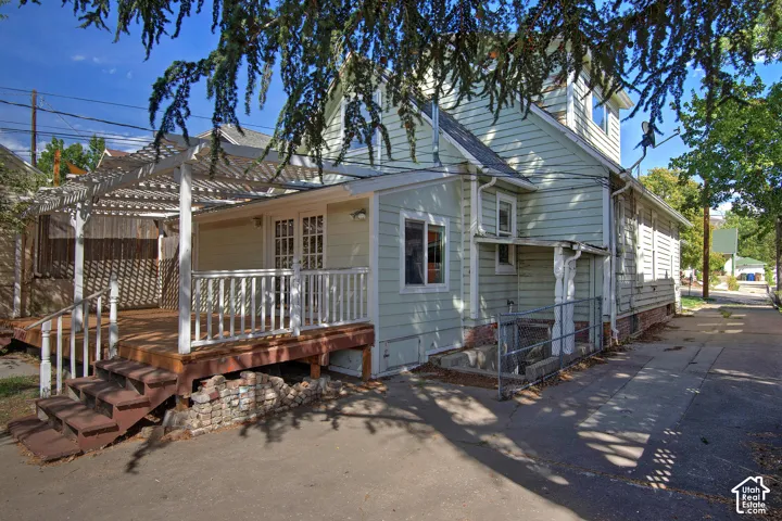 Exterior featuring light-colored siding, a multi-level wood deck with steps, a white pergola structure, and white French doors