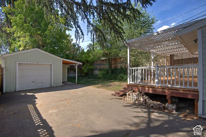 Detached garage with covered entryway, concrete driveway, and elevated wood deck with white lattice pergola and railing